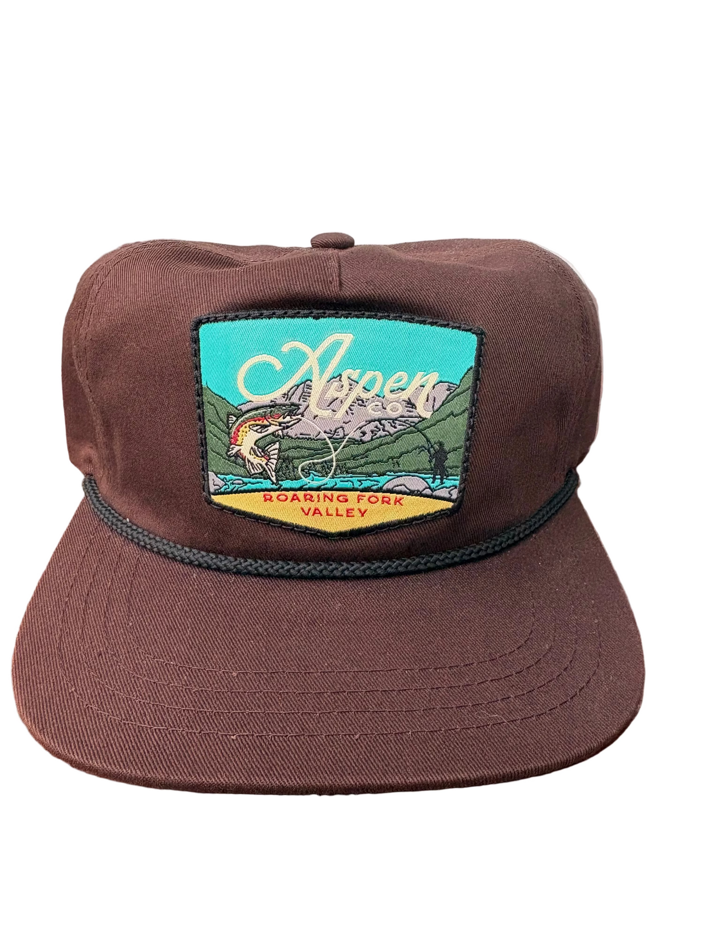 Brown cap with a colorful patch featuring a mountain and river scene on a wooden surface.