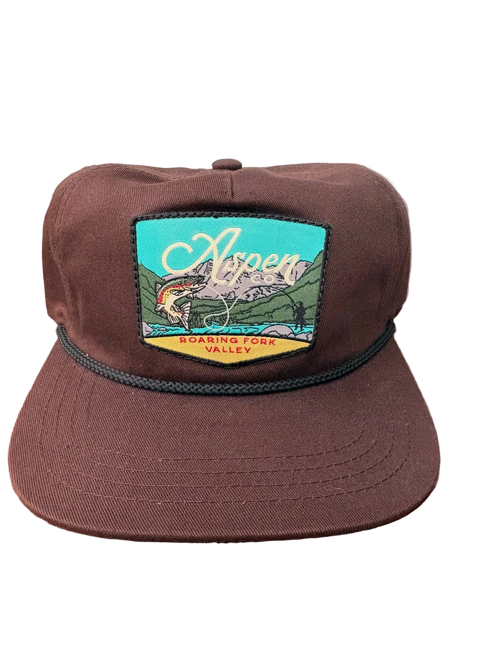 Brown cap with a colorful patch featuring a mountain and river scene on a wooden surface.